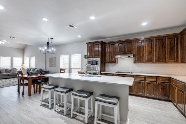 kitchen featuring a center island with sink, stainless steel appliances, light countertops, a sink, and under cabinet range hood