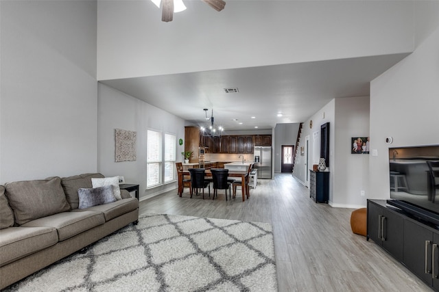 living room featuring light wood-type flooring, visible vents, baseboards, and ceiling fan with notable chandelier