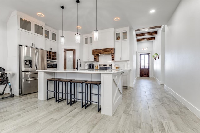 kitchen featuring stainless steel appliances, light countertops, backsplash, glass insert cabinets, and an island with sink