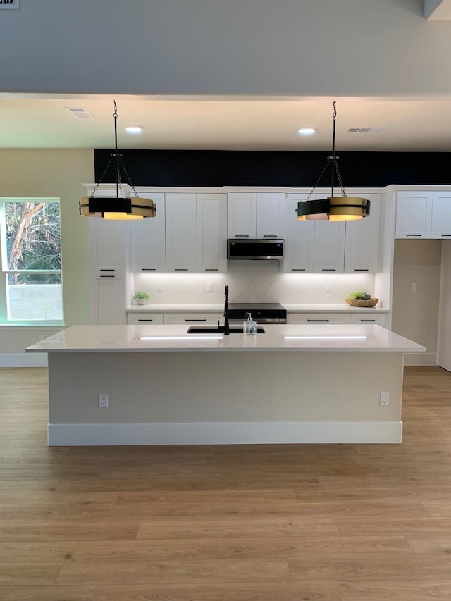 kitchen with light countertops, pendant lighting, a kitchen island with sink, and exhaust hood