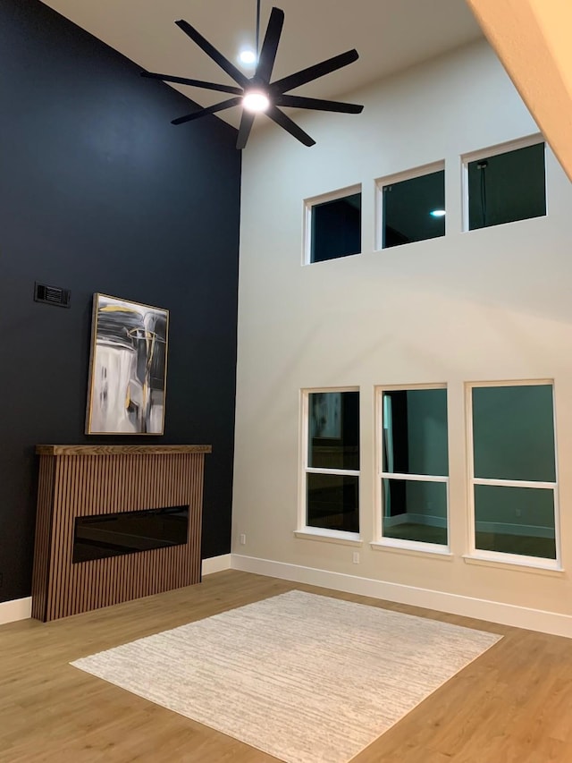 unfurnished living room featuring visible vents, a towering ceiling, baseboards, and wood finished floors