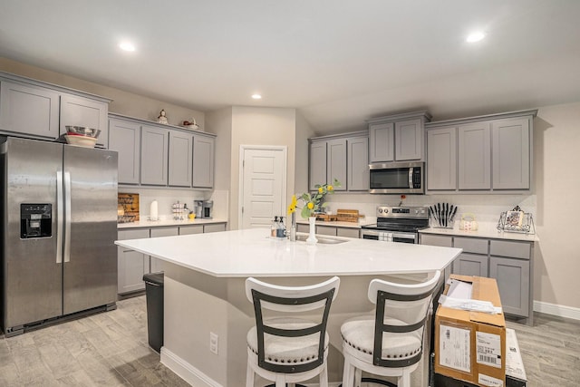 kitchen featuring gray cabinetry, light countertops, appliances with stainless steel finishes, an island with sink, and a kitchen bar