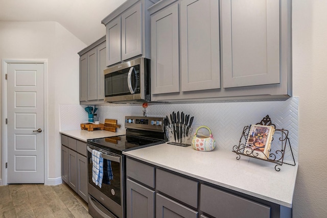 kitchen with light wood-style flooring, stainless steel appliances, light countertops, gray cabinets, and backsplash