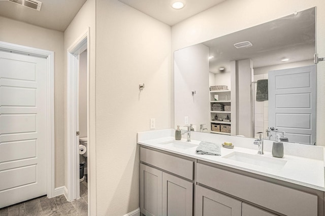 bathroom featuring toilet, double vanity, a sink, and visible vents