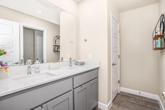 full bath with double vanity, a sink, baseboards, and wood finished floors