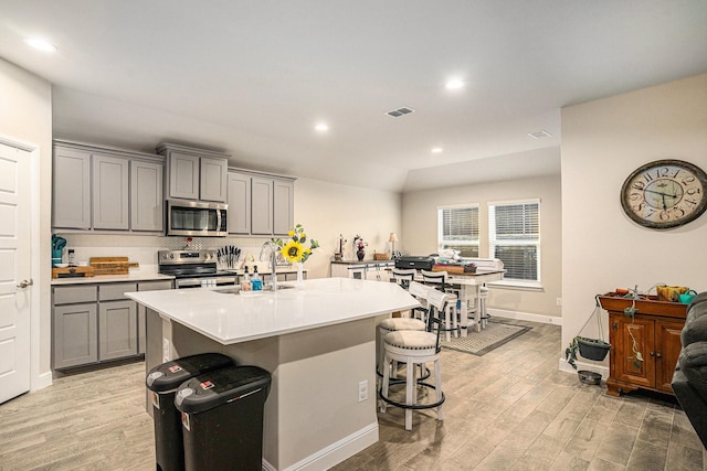 kitchen featuring stainless steel appliances, a breakfast bar, light countertops, and gray cabinetry