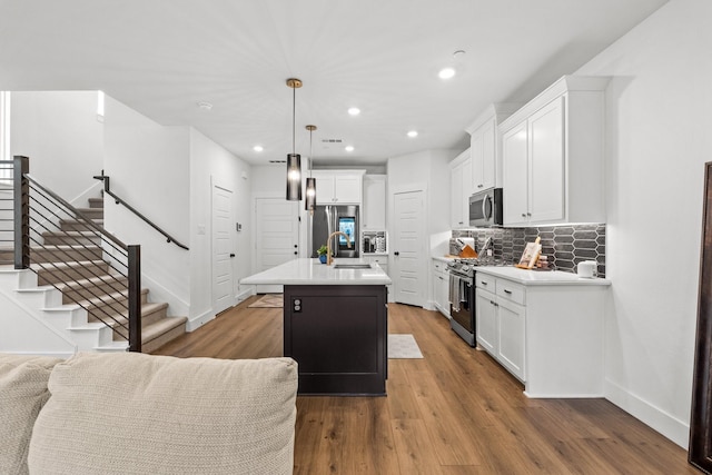 kitchen featuring a center island with sink, white cabinets, appliances with stainless steel finishes, hanging light fixtures, and light countertops