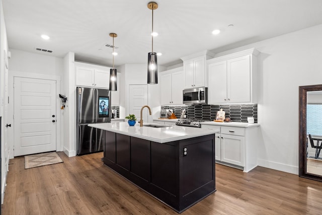 kitchen with light countertops, appliances with stainless steel finishes, a center island with sink, and white cabinets