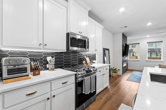 kitchen with dark wood-style flooring, stainless steel appliances, visible vents, white cabinetry, and light stone countertops