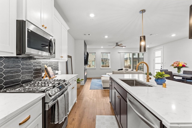 kitchen featuring light stone counters, stainless steel appliances, hanging light fixtures, white cabinets, and a sink