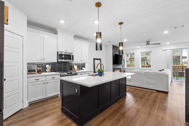 kitchen with a center island with sink, light countertops, appliances with stainless steel finishes, open floor plan, and a sink