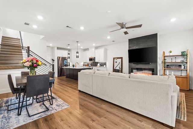 living area featuring a tile fireplace, light wood-style flooring, recessed lighting, a ceiling fan, and stairway