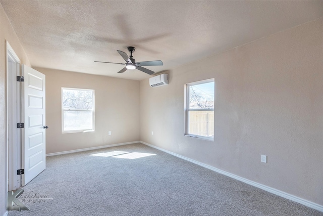 carpeted spare room featuring a textured wall, a wall mounted AC, ceiling fan, a textured ceiling, and baseboards