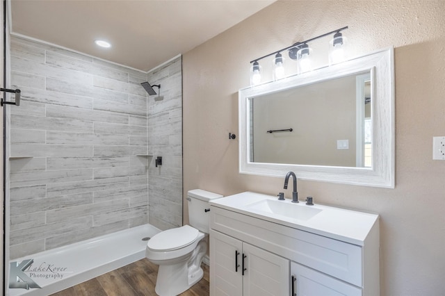 full bath featuring toilet, a tile shower, wood finished floors, and vanity