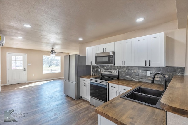 kitchen featuring white cabinets, butcher block counters, stainless steel appliances, and a sink