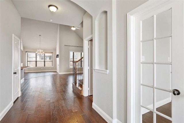 hall with lofted ceiling, a notable chandelier, dark wood-type flooring, baseboards, and stairway