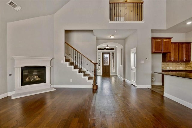 foyer with arched walkways, dark wood-style flooring, visible vents, baseboards, and a glass covered fireplace