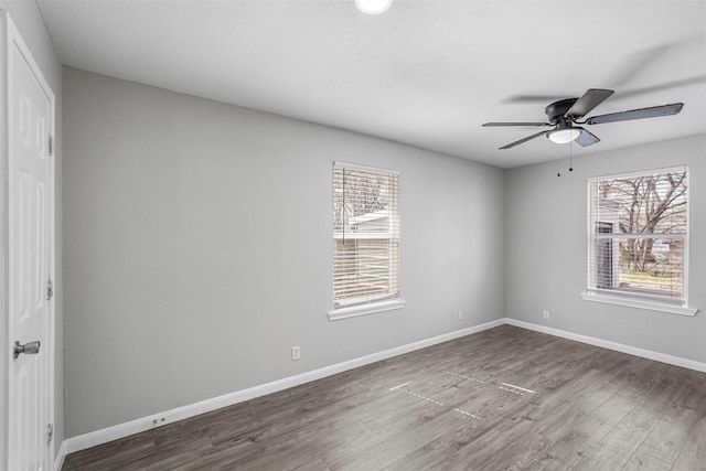 spare room featuring dark wood finished floors, plenty of natural light, a ceiling fan, and baseboards