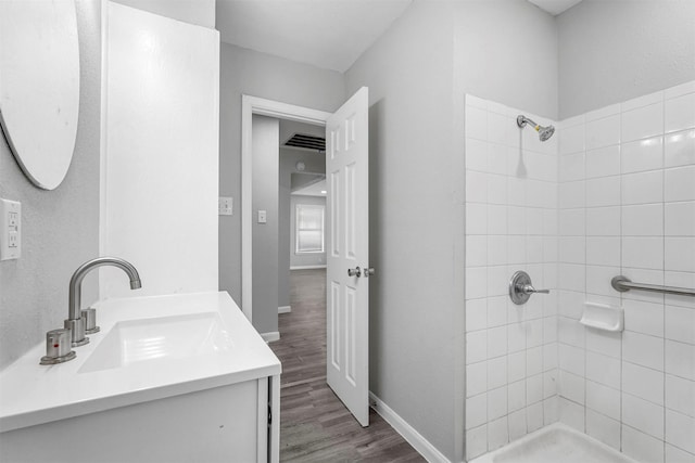 bathroom featuring visible vents, wood finished floors, baseboards, tiled shower, and vanity