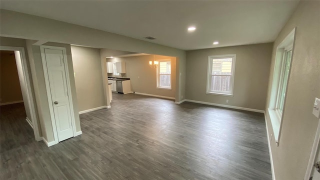 unfurnished living room with dark wood-style floors, recessed lighting, baseboards, and an inviting chandelier