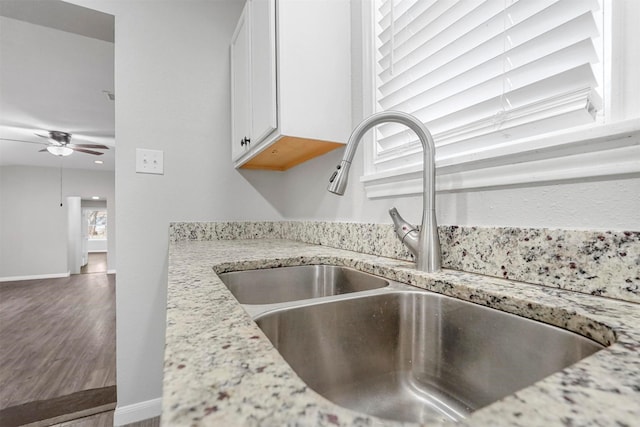 details with a sink, white cabinetry, baseboards, ceiling fan, and light stone countertops