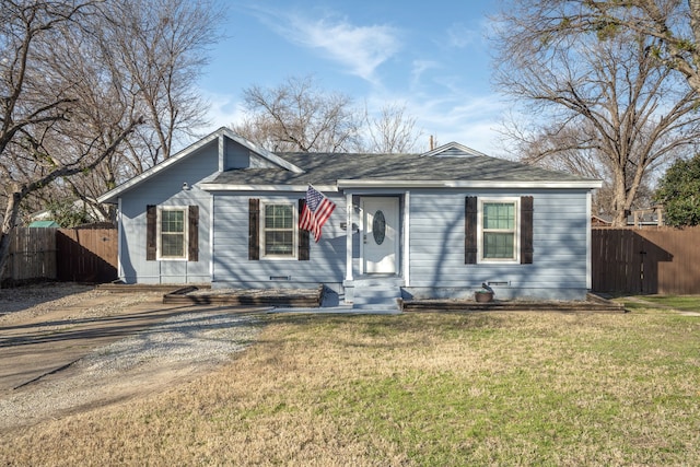 view of front of house featuring roof with shingles, dirt driveway, fence, and a front yard