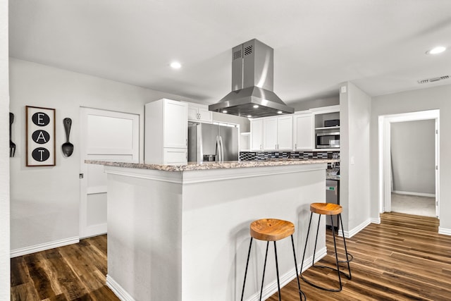 kitchen with island range hood, a kitchen island, white cabinets, appliances with stainless steel finishes, and backsplash