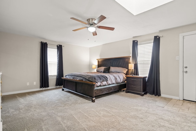 bedroom featuring light carpet, a skylight, baseboards, and a ceiling fan