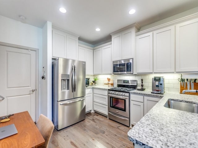 kitchen featuring light stone countertops, stainless steel appliances, light wood-type flooring, white cabinetry, and backsplash