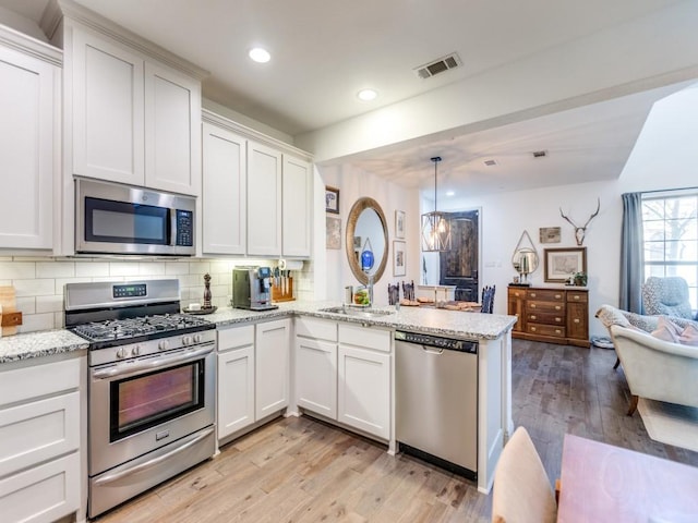 kitchen featuring stainless steel appliances, pendant lighting, white cabinets, and a peninsula