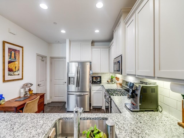 kitchen featuring appliances with stainless steel finishes, white cabinetry, a sink, and light stone counters