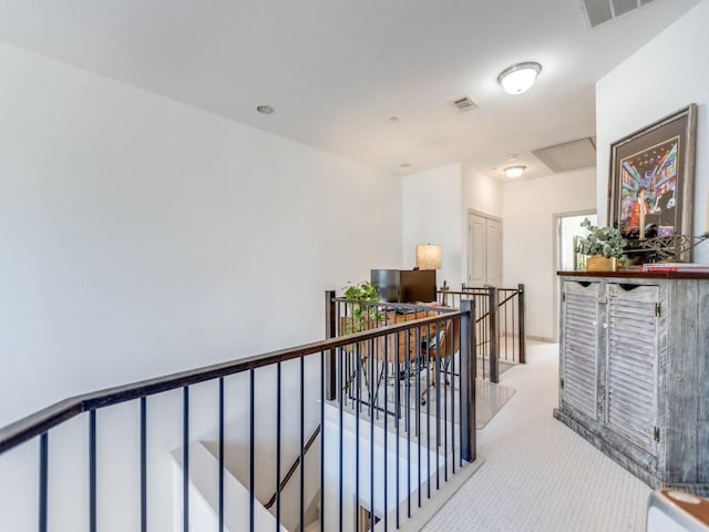 hallway with light carpet, visible vents, and an upstairs landing