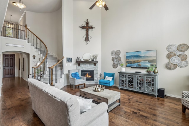 living area featuring a stone fireplace, dark wood finished floors, stairway, and baseboards