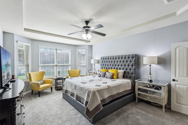 bedroom with a textured ceiling, a raised ceiling, carpet flooring, and a ceiling fan