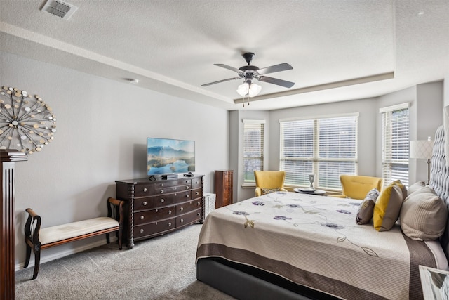 carpeted bedroom featuring a textured ceiling, a tray ceiling, visible vents, and a ceiling fan