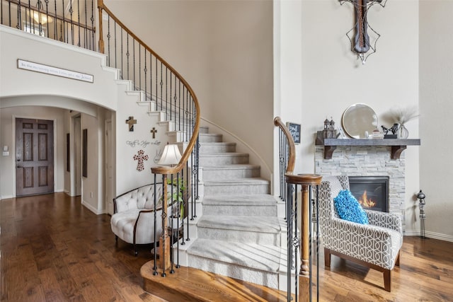 entryway featuring a towering ceiling, a fireplace, arched walkways, and wood finished floors