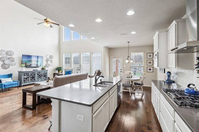 kitchen featuring hanging light fixtures, open floor plan, a sink, wall chimney range hood, and an island with sink