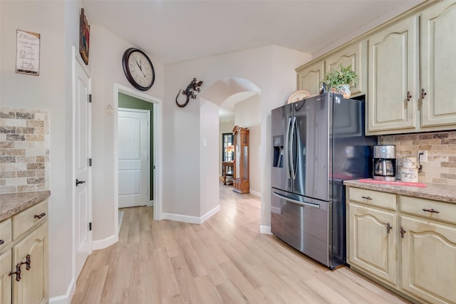 kitchen featuring tasteful backsplash, light wood-type flooring, cream cabinets, stainless steel refrigerator with ice dispenser, and arched walkways