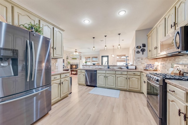 kitchen featuring appliances with stainless steel finishes, a peninsula, light wood-style flooring, ceiling fan, and decorative backsplash