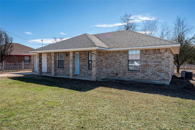 back of house featuring a shingled roof, brick siding, a yard, and central AC unit