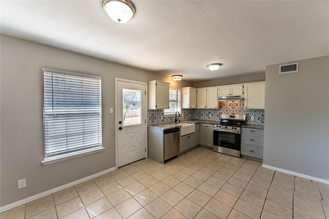 kitchen with stainless steel appliances, visible vents, backsplash, a sink, and baseboards