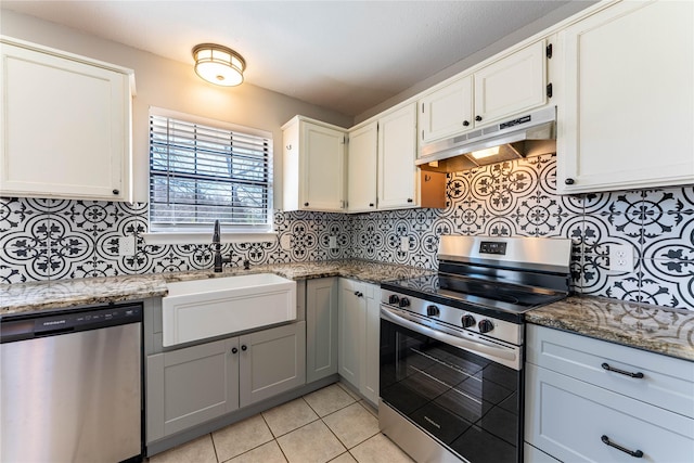 kitchen featuring dark stone counters, appliances with stainless steel finishes, under cabinet range hood, white cabinetry, and a sink