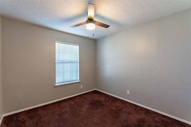 empty room with a textured ceiling, dark carpet, a ceiling fan, and baseboards