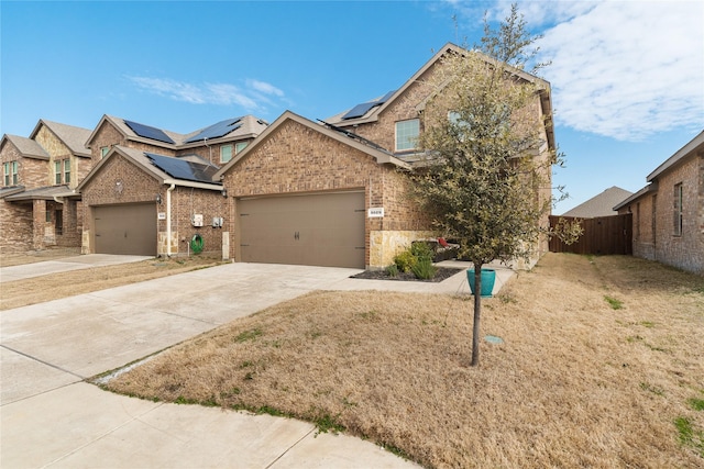 view of front of home with brick siding, concrete driveway, an attached garage, roof mounted solar panels, and fence