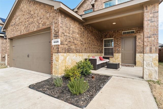 view of exterior entry with a garage, concrete driveway, brick siding, and an outdoor living space