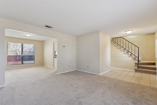 spare room featuring light tile patterned floors, a textured ceiling, light colored carpet, visible vents, and stairway