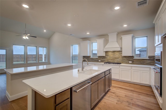 kitchen featuring stainless steel appliances, a kitchen island with sink, custom range hood, and a sink