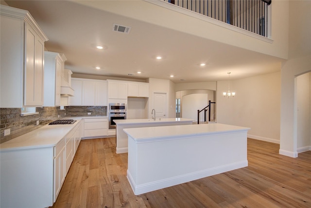 kitchen with visible vents, appliances with stainless steel finishes, a kitchen island with sink, light countertops, and white cabinetry