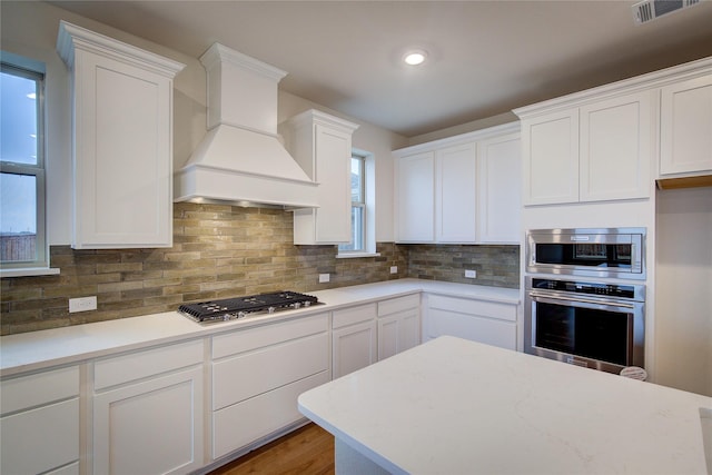 kitchen featuring visible vents, white cabinetry, appliances with stainless steel finishes, custom exhaust hood, and decorative backsplash