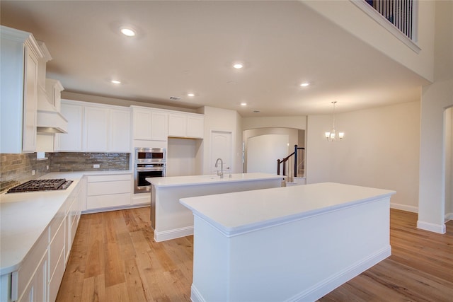 kitchen with white cabinets, a kitchen island with sink, stainless steel appliances, and light countertops